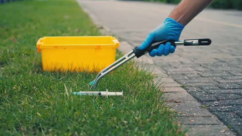 Discarded syringe being lifted with a litter picker into a sharps container during a needle sweep